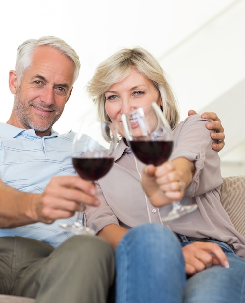Coppie mature sorridenti con i vetri di vino che si siedono sul sofà