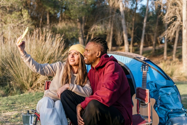 Coppie multirazziali felici che prendono selfie vicino alla tenda