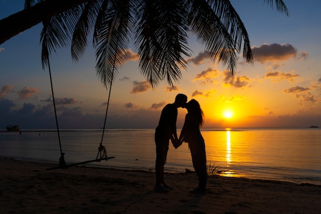 Coppie profilate nei baci di amore sulla spiaggia durante il tramonto.