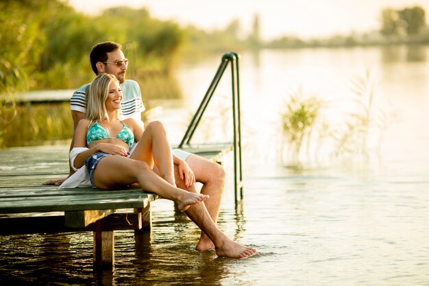 Coppie romantiche che si siedono sul pilastro di legno sul lago