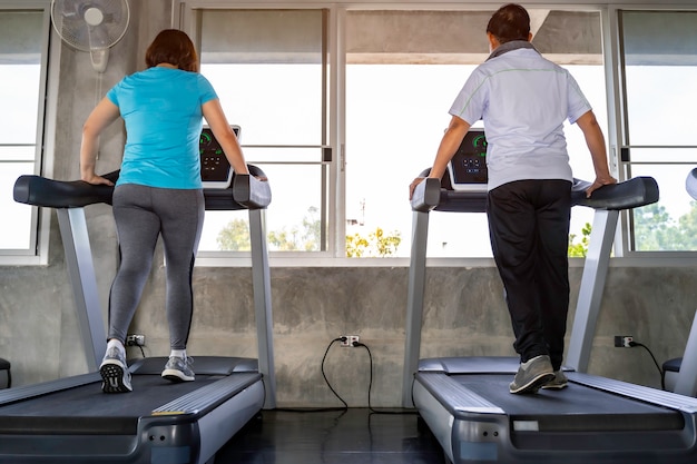 Coppie senior asiatiche che sorridono in abiti sportivi che si esercitano alla palestra.