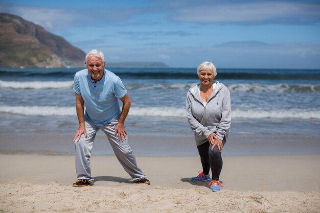 Coppie senior che fanno allungando esercizio sulla spiaggia