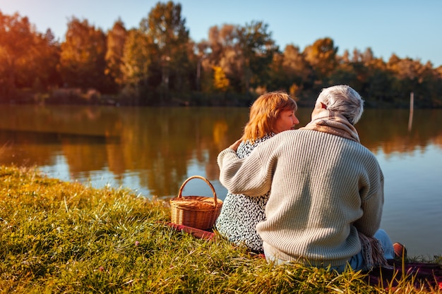 Coppie senior che hanno picnic dal lago di autunno Abbracciare felice della donna e dell&#39;uomo