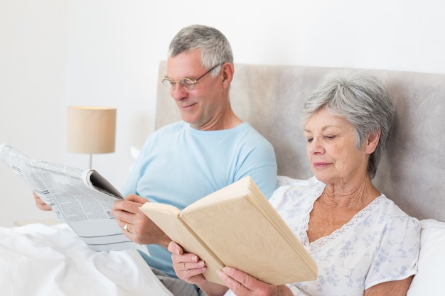 Coppie senior che leggono giornale e libro a letto