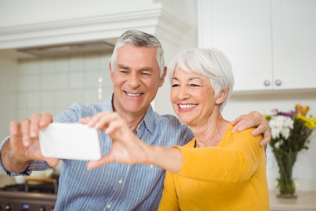 Coppie senior che prendono selfie dal telefono cellulare in cucina