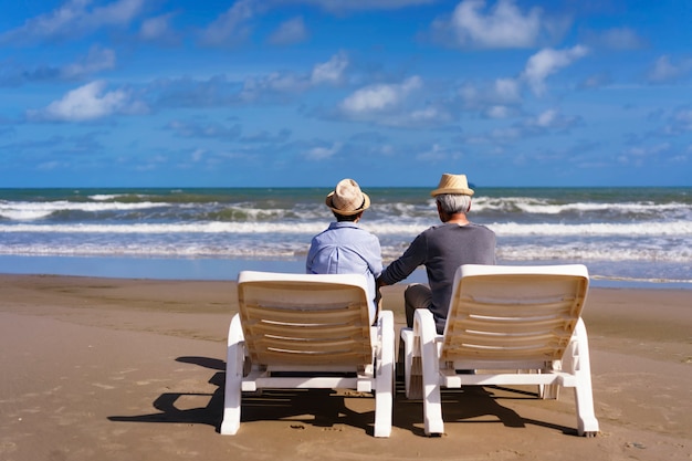 Coppie senior che si siedono sugli sdrai sulla spiaggia