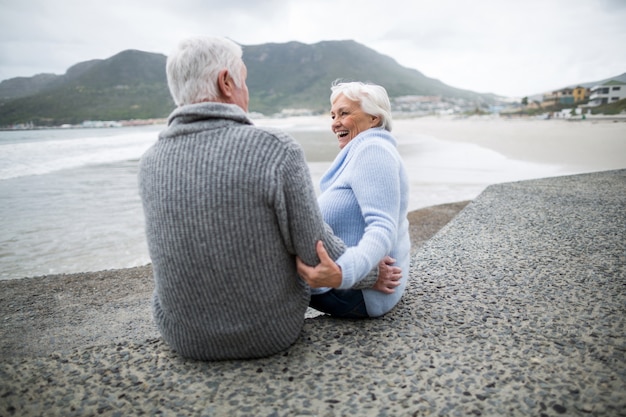 Coppie senior che si siedono sulla roccia alla spiaggia