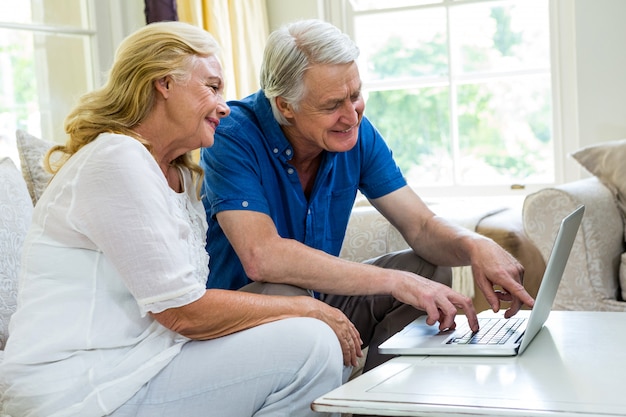 Coppie senior che utilizzano computer portatile mentre sedendosi nel salone a casa