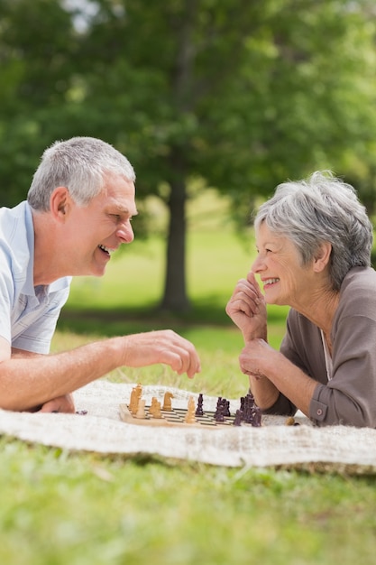 Coppie senior felici che giocano scacchi al parco