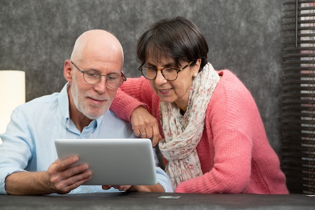 Coppie senior felici facendo uso della compressa digitale