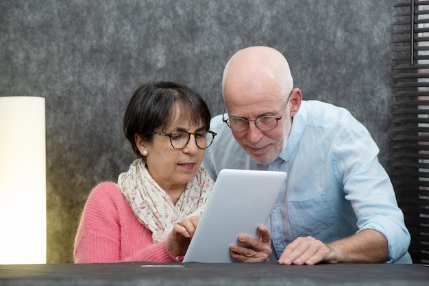 Coppie senior felici facendo uso della compressa digitale