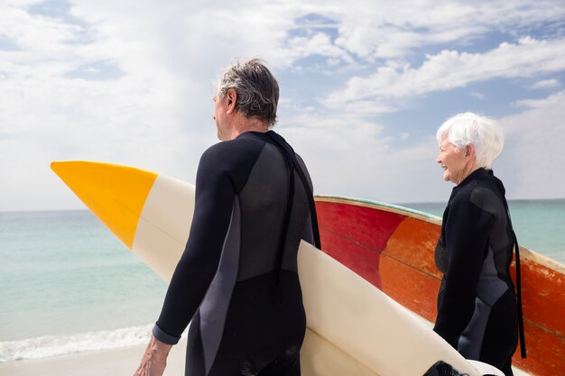 Coppie senior nel surf della tenuta della muta umida sulla spiaggia