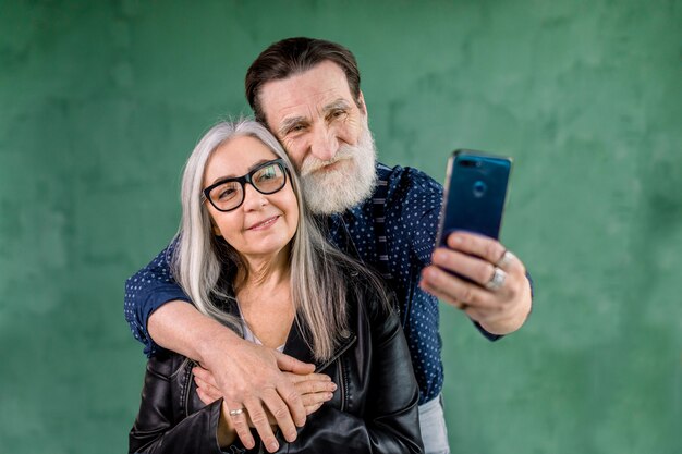 Coppie senior soddisfatte sorridenti che esaminano insieme la macchina fotografica del telefono per la presa della foto del selfie