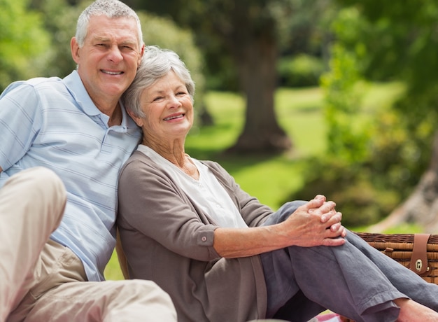 Coppie senior sorridenti che si siedono con il canestro di picnic al parco