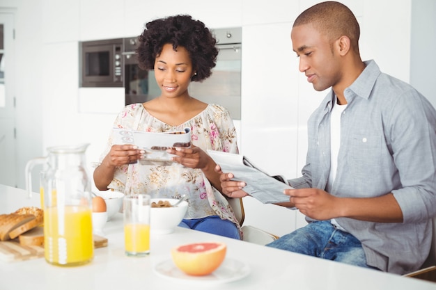 Coppie sorridenti che leggono rivista e documenti durante la prima colazione in cucina