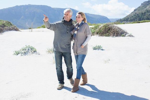 Coppie sorridenti che passeggiano sulla spiaggia in vestiti caldi