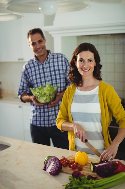 Coppie sorridenti che tagliano le verdure a pezzi nella cucina a casa