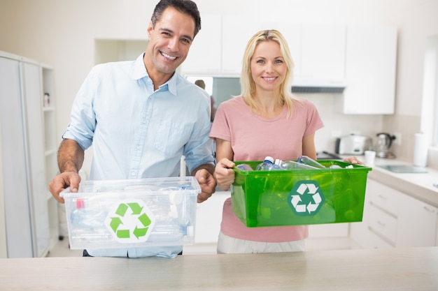 Coppie sorridenti che trasportano i contenitori di riciclaggio in cucina