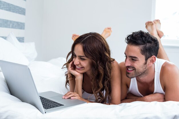 Coppie sorridenti facendo uso del computer portatile mentre trovandosi sotto la coperta