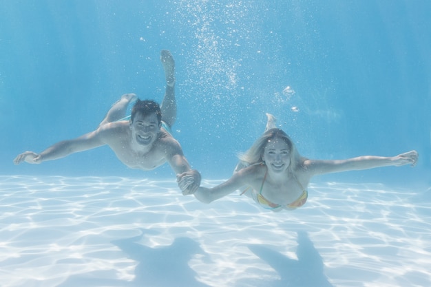 Coppie sveglie che sorridono alla macchina fotografica subacquea nella piscina