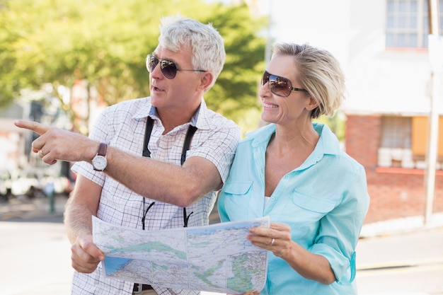 Coppie turistiche felici facendo uso della mappa nella città