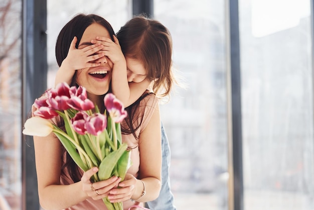 Coprendo gli occhi La figlia si congratula con la madre per le vacanze e regala un mazzo di fiori