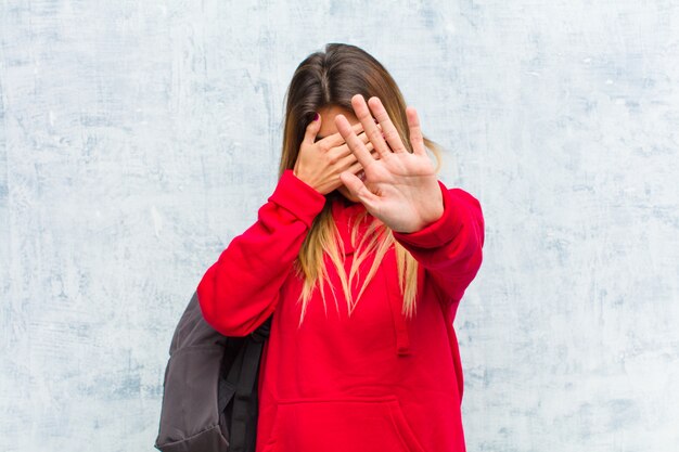 coprendo il viso con la mano e mettendo l'altra mano in avanti per fermare la fotocamera, rifiutando foto o immagini