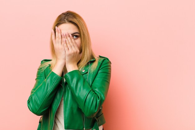 coprendo il viso con le mani, sbirciando tra le dita con espressione sorpresa e guardando di lato