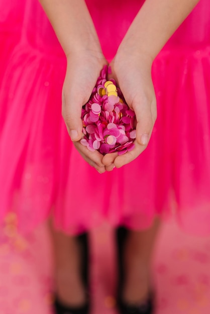 Coriandoli di carta rosa e oro brillante nei palmi di una ragazza di compleanno in un vestito a una festa