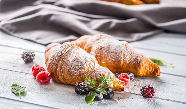 Cornetti appena croccanti spolverati di zucchero a velo con lampone mora e mirtillo con foglie di mellisa.