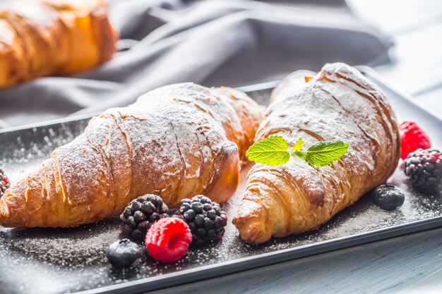 Cornetti appena croccanti spolverati di zucchero a velo con lampone mora e mirtillo con foglie di mellisa.