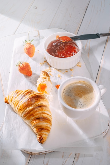 Cornetti appena sfornati freschi con marmellata e caffè sul tavolo al sole del mattino. concetto di deliziosa colazione