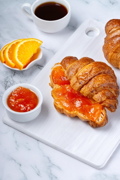 Cornetti dolci freschi con burro e marmellata di albicocche per colazione Colazione continentale su fondo bianco