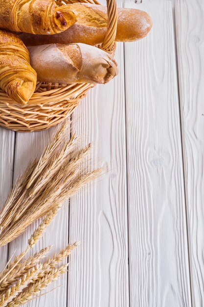 Cornetti e baguette in cesto di vimini spighe di grano su tavole di legno bianche con copyspace