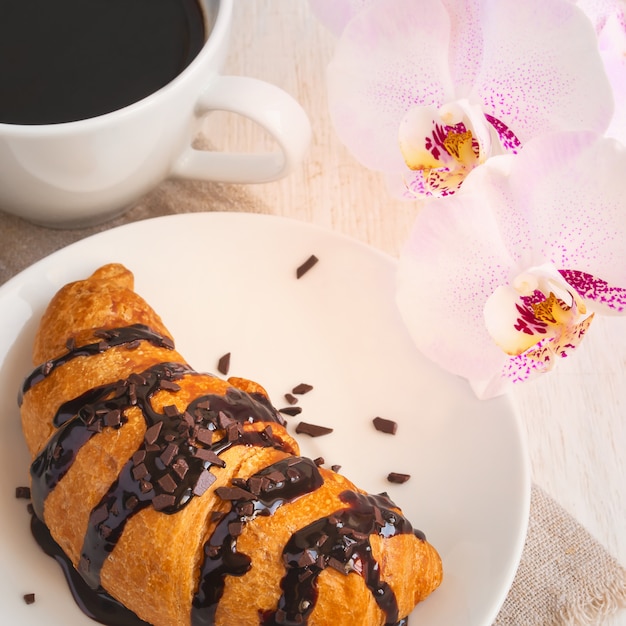 Cornetto al cioccolato, tazza di caffè e un'orchidea rosa.