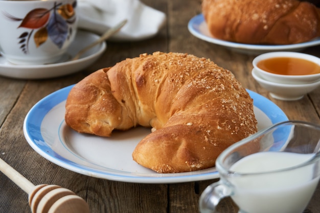 Cornetto fresco, una tazza di caffè e miele su un tavolo di legno