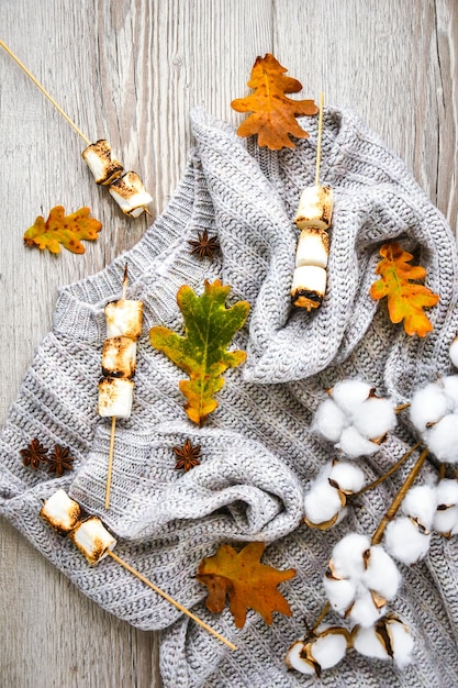 Cornice autunnale fatta di foglie d'autunno, marshmallow, noci, cannella, maglione di cotone. Vista dall'alto su uno sfondo di legno. Composizione autunnale. Ornamento per il Ringraziamento