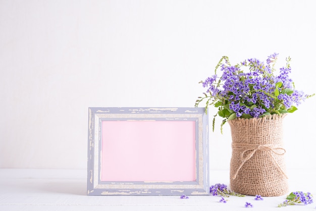 Cornice bianca con il fiore porpora adorabile in vaso sulla tavola di legno bianca.