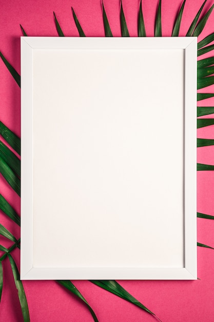 Cornice bianca con il modello vuoto sulle foglie di palma, fondo rosa-rosso