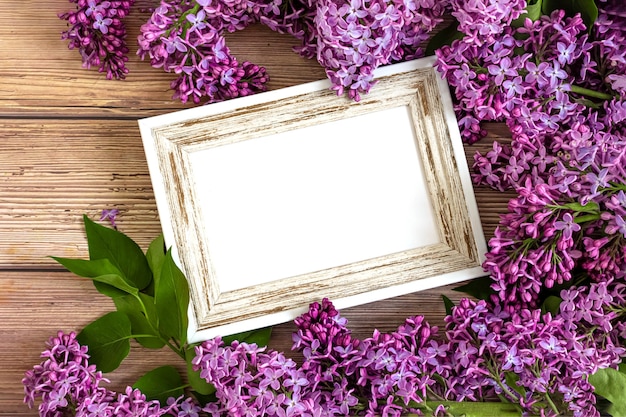 Cornice bianca decorata con fiori lilla in fiore su fondo di legno rustico. Invito o biglietto di auguri per San Valentino e la festa della mamma. Vista dall'alto, distesi, copia spazio. concetto di primavera.