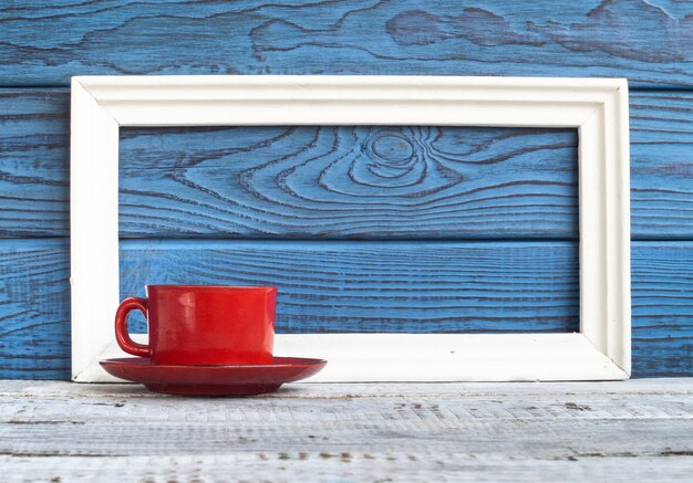 Cornice bianca e tazza di caffè rossa su uno sfondo di tavole blu