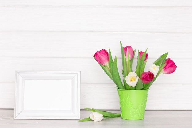 Cornice bianca vuota con bouquet di fiori di tulipano sul tavolo vicino al muro Sfondo di mockup di primavera