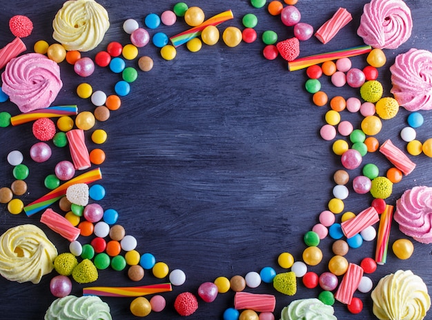 Cornice colorata di caramelle multicolore su fondo di legno nero