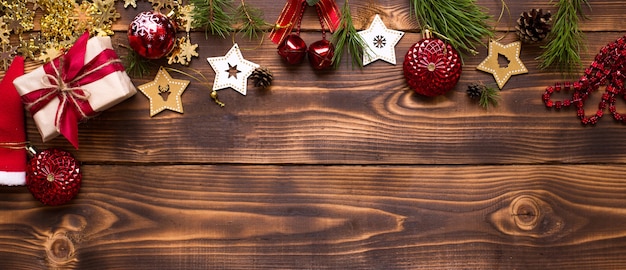 Cornice con decorazioni natalizie su uno sfondo di legno. Anno nuovo, atmosfera vacanziera, rami di abete verde, decorazioni: stelle, confezione regalo, perline, palline, campanelli, coni. Spazio per il testo, piatto laici
