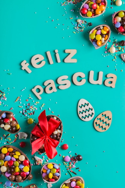 Cornice di Pasqua con uova di cioccolato e dolci su sfondo turchese, verde, blu. Feliz Pascua - testo di buona pasqua in spagnolo. Vista dall'alto, distesa