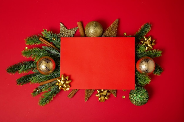 Cornice di rami di albero di Natale e decorazioni con carta bianca e spazio per il testo di sfondo rosso