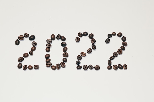Cornice di sfondo di chicchi di caffè figure del nuovo anno 2022 disposte su uno sfondo bianco di chicchi di caffè...