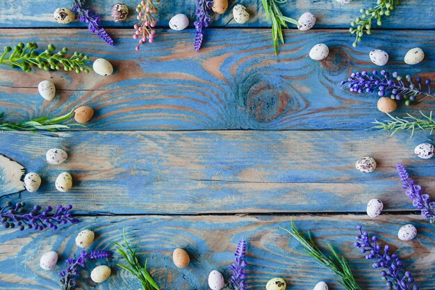 Cornice di uova di quaglia e fiori di salvia su un tavolo di legno blu consumato.