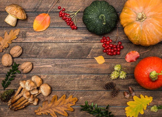 Cornice festiva autunnale con zucche bacche funghi noci e foglie su fondo di legno rustico Concetto di giorno del Ringraziamento Composizione autunnale piatta con spazio di copia