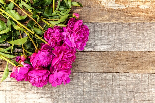 Cornice floreale con bouquet di fiori di peonia rosa magenta in fiore fresco su vecchio fondo di legno rustico misero, copyspace